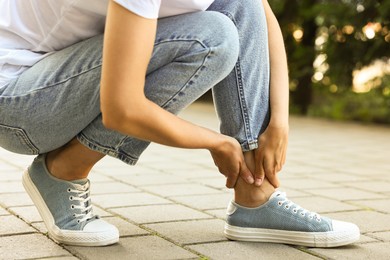 Photo of Woman suffering from foot pain outdoors, closeup