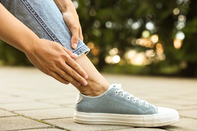 Photo of Woman suffering from foot pain outdoors, closeup