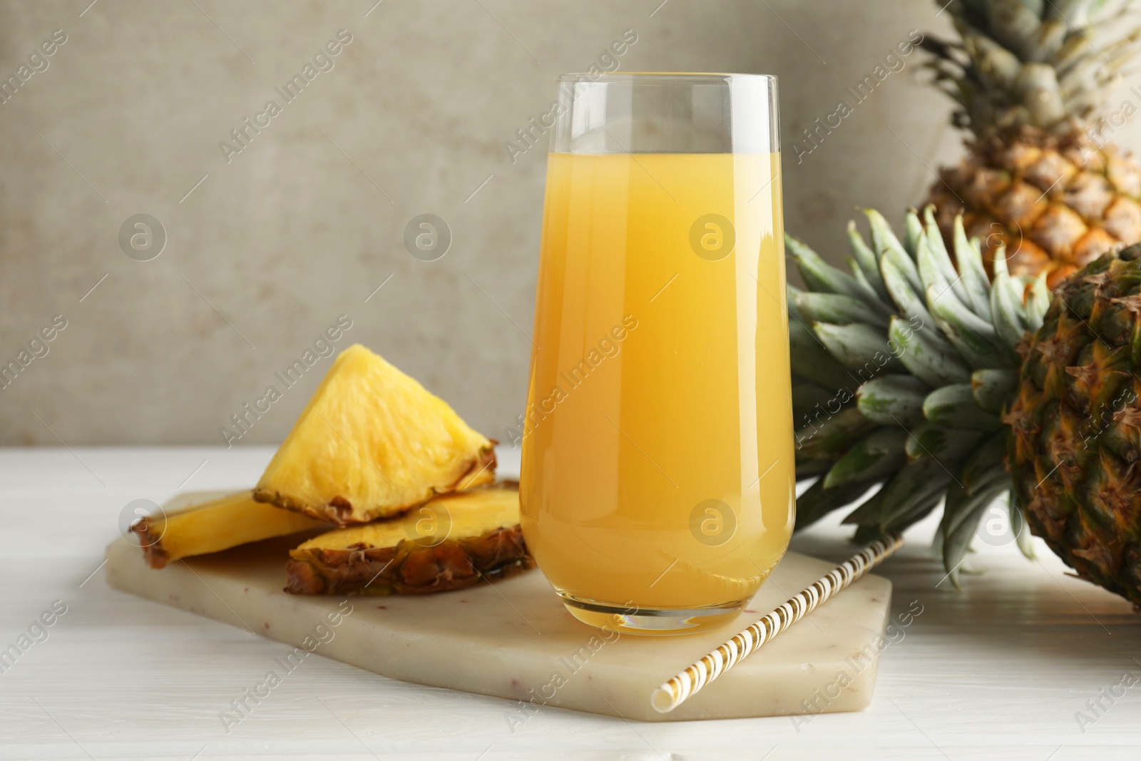 Photo of Tasty pineapple juice in glass and fresh fruits on white wooden table against grey background, closeup