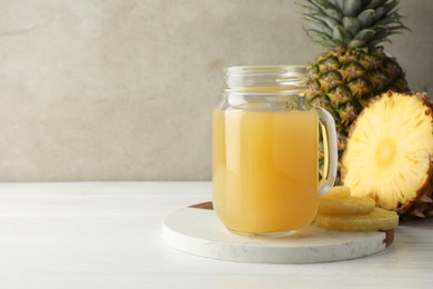 Photo of Tasty pineapple juice in mason jar and fresh fruits on white wooden table against grey background, closeup. Space for text