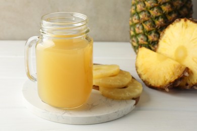 Photo of Tasty pineapple juice in mason jar and fresh fruits on white wooden table against grey background, closeup