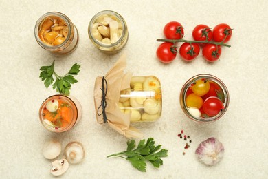 Photo of Different pickled products in jars and fresh ingredients on beige textured table, flat lay