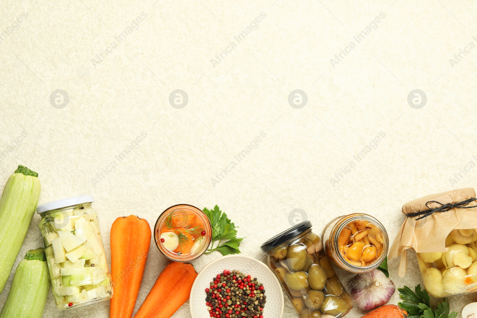 Photo of Different pickled products in jars and fresh ingredients on beige textured table, flat lay. Space for text