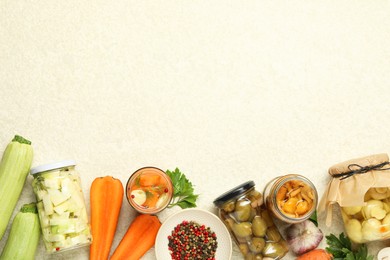 Photo of Different pickled products in jars and fresh ingredients on beige textured table, flat lay. Space for text