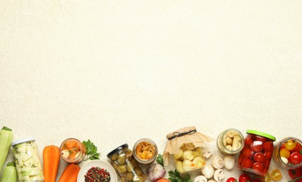 Photo of Different pickled products in jars and fresh ingredients on beige textured table, flat lay. Space for text