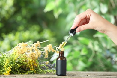 Photo of Woman dripping tincture from pipette into bottle at wooden table against blurred green background, closeup