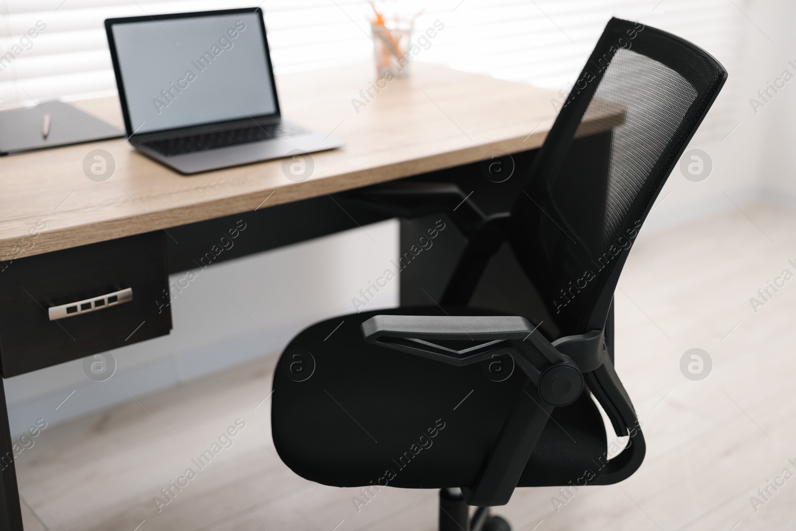 Photo of Black chair, laptop and desk in office, closeup