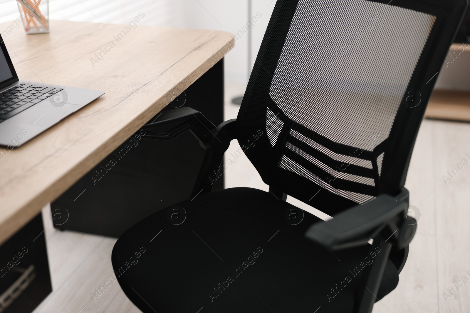 Photo of Black chair, laptop and desk in office, closeup