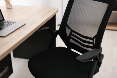 Black chair, laptop and desk in office, closeup