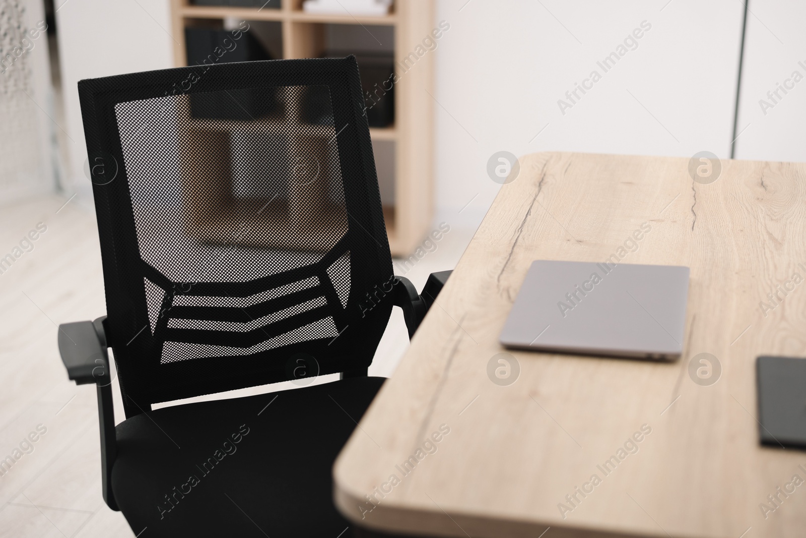 Photo of Black chair, laptop and desk in office, closeup