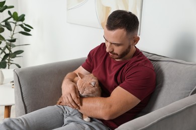 Photo of Man petting cute ginger cat on armchair at home