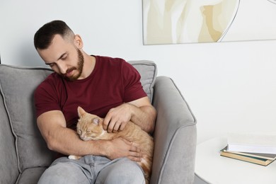 Man petting cute ginger cat on armchair at home, space for text