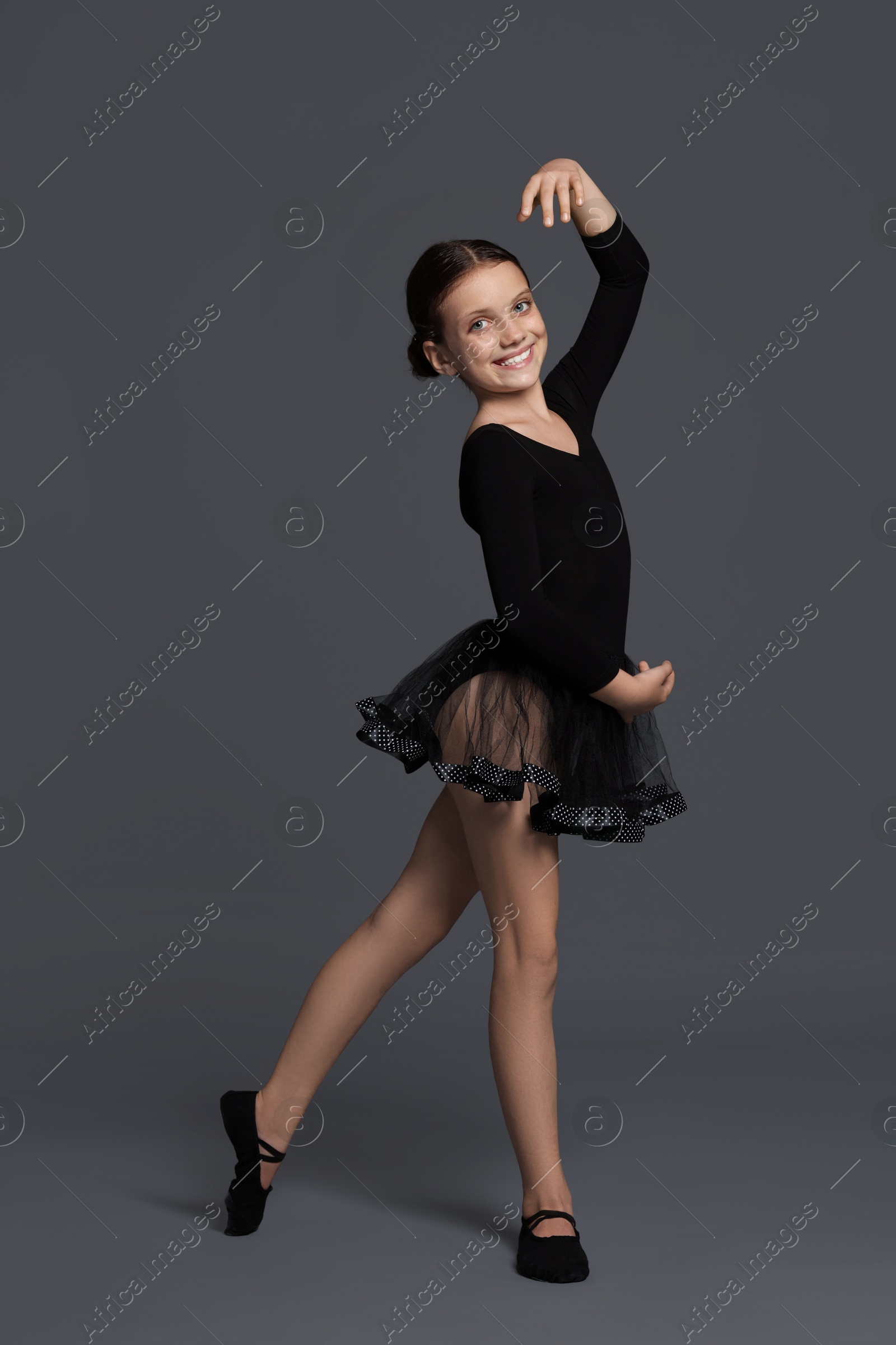 Photo of Little ballerina practicing dance moves on grey background