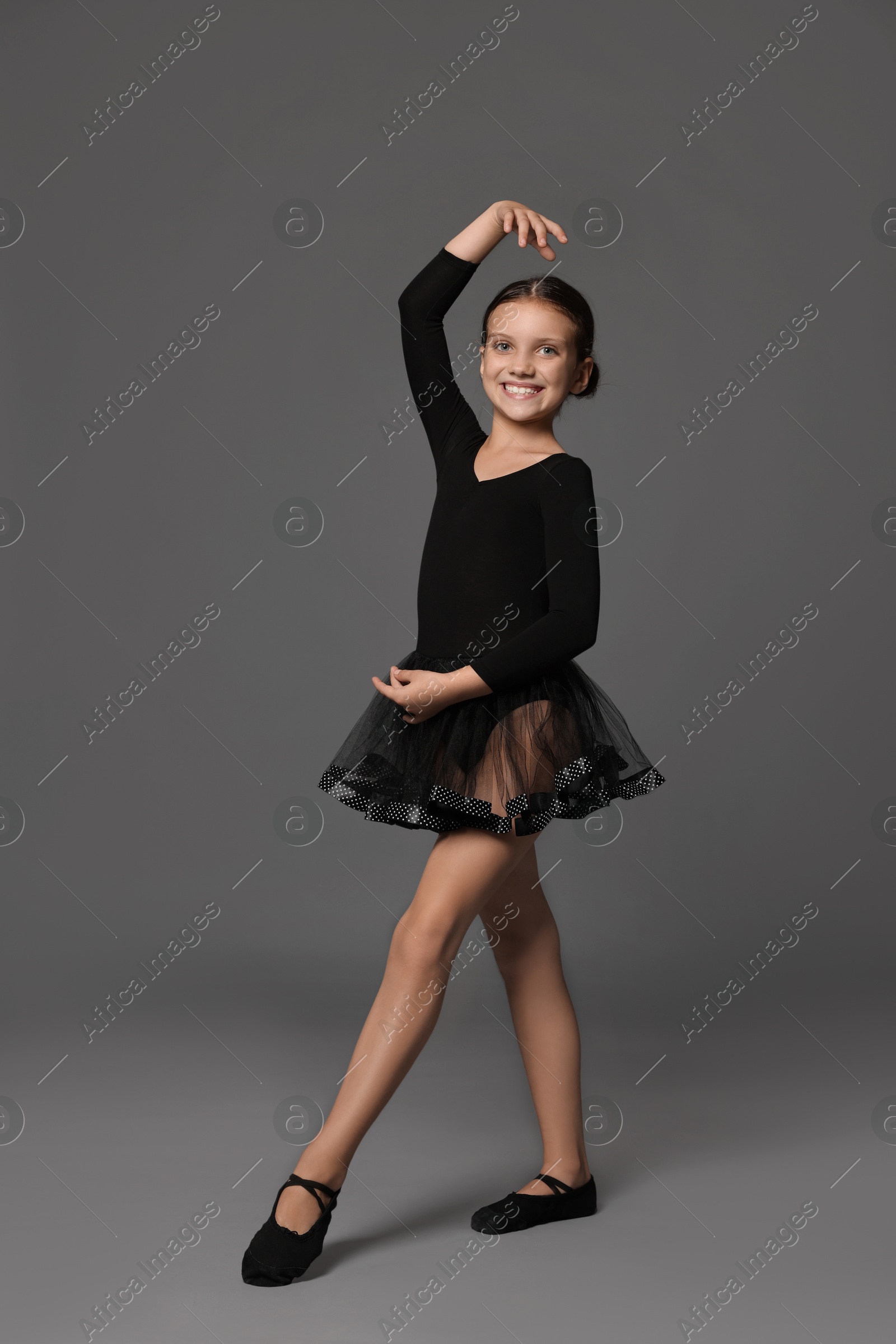 Photo of Little ballerina practicing dance moves on grey background