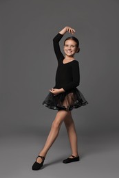 Little ballerina practicing dance moves on grey background