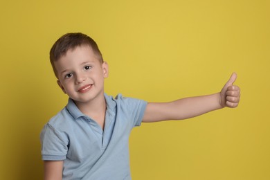 Photo of Cute little boy showing thumbs up on yellow background