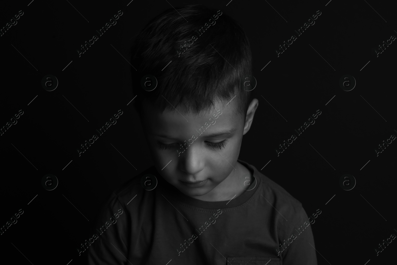 Photo of Portrait of sad little boy on dark background. Black and white effect