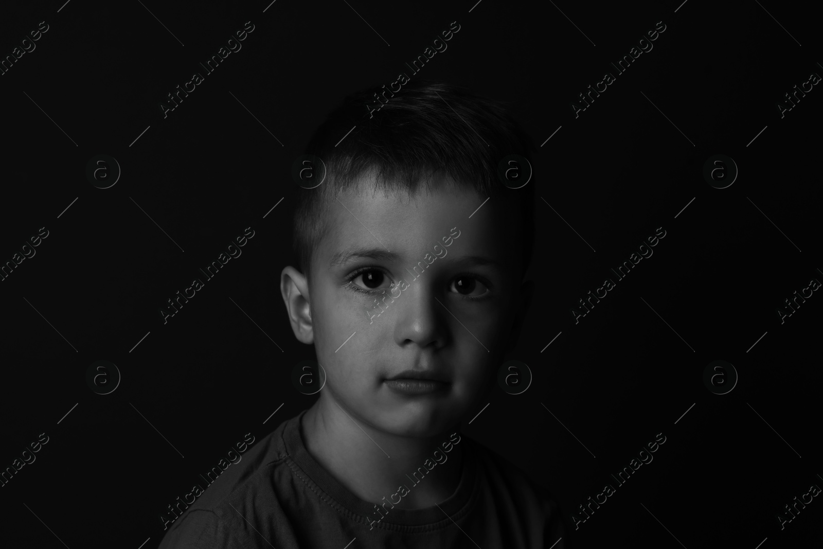 Photo of Portrait of sad little boy on dark background. Black and white effect