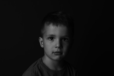 Portrait of sad little boy on dark background. Black and white effect