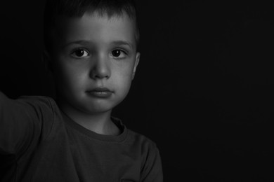 Portrait of sad little boy on dark background, space for text. Black and white effect