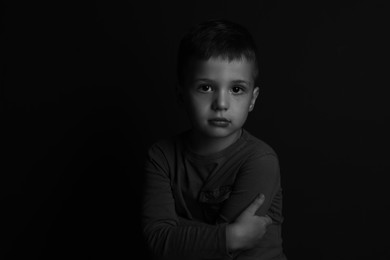 Portrait of sad little boy on dark background. Black and white effect