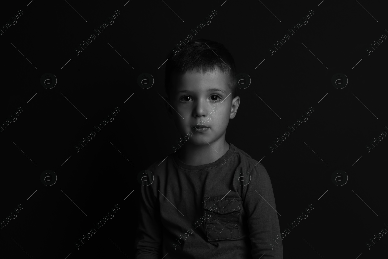 Photo of Portrait of sad little boy on dark background. Black and white effect