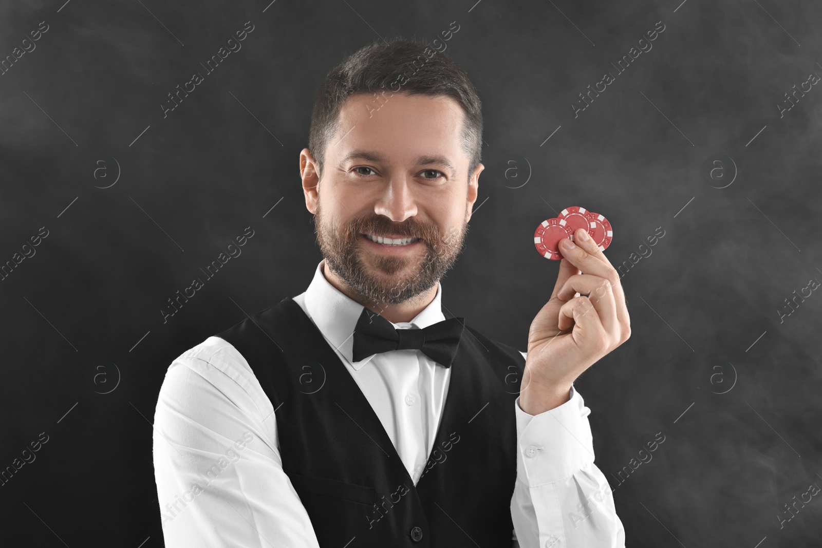 Photo of Croupier holding casino chips on black background with smoke