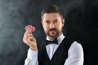 Photo of Croupier holding casino chips on black background with smoke