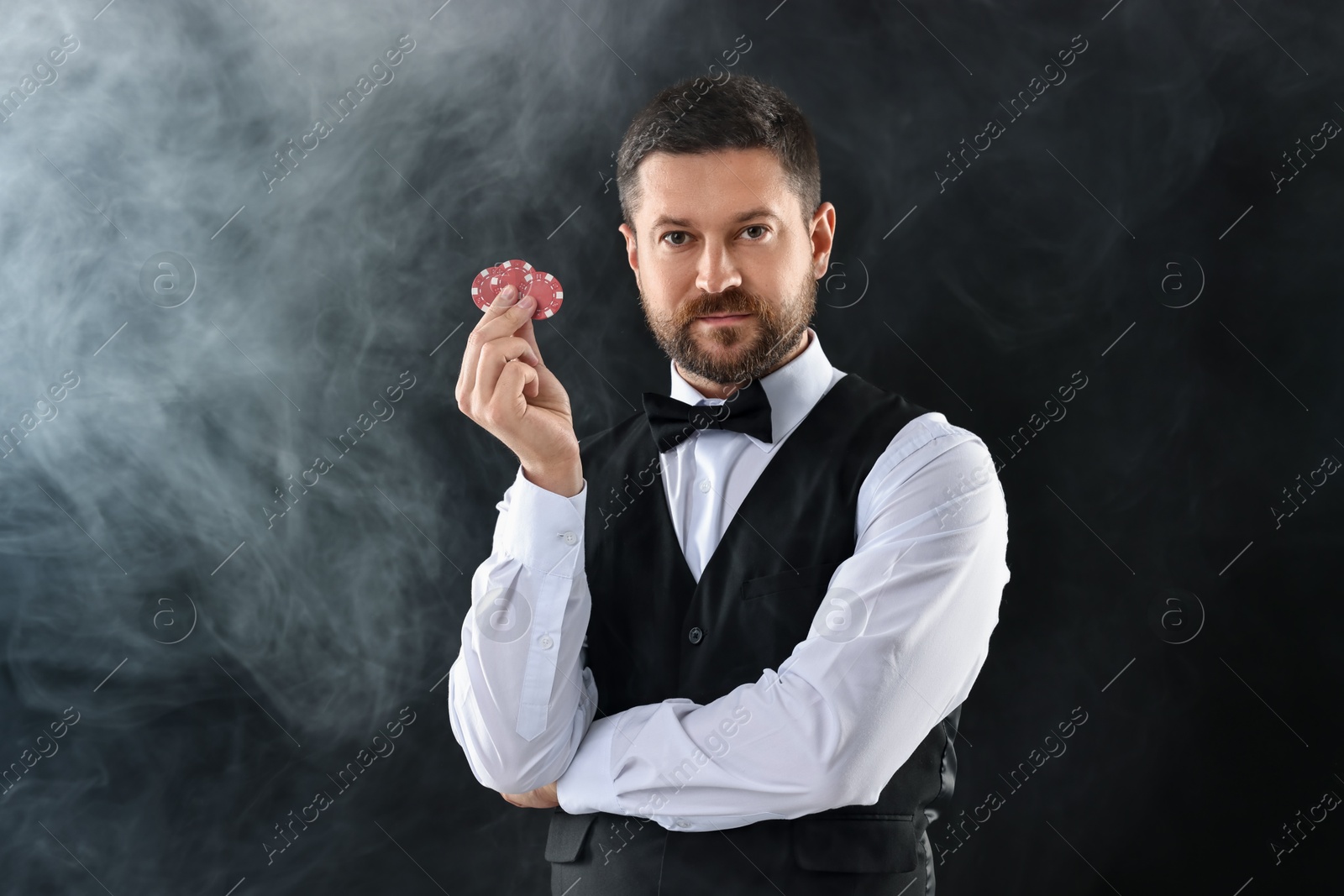 Photo of Croupier holding casino chips on black background with smoke