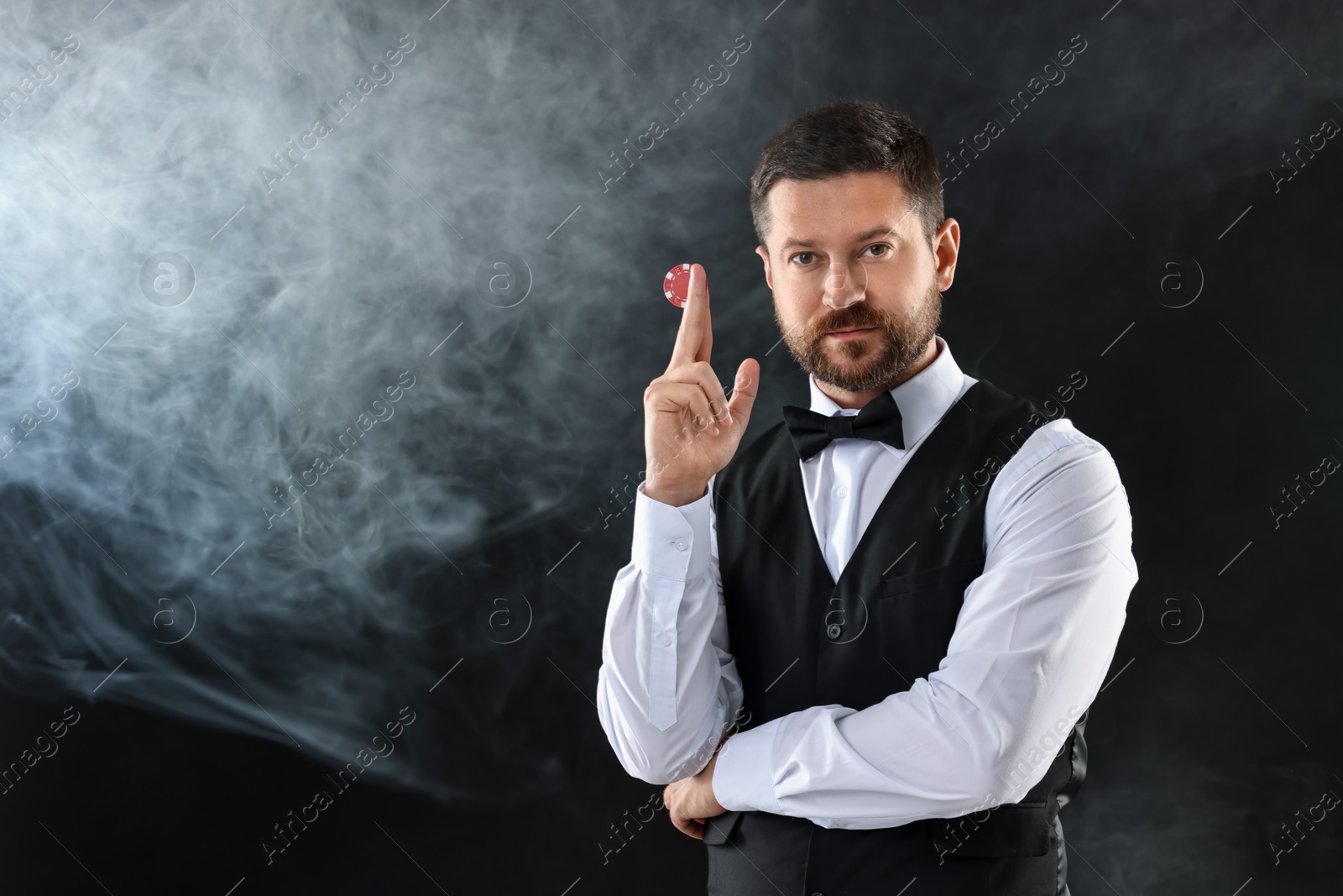 Photo of Croupier holding casino chip on black background with smoke, space for text