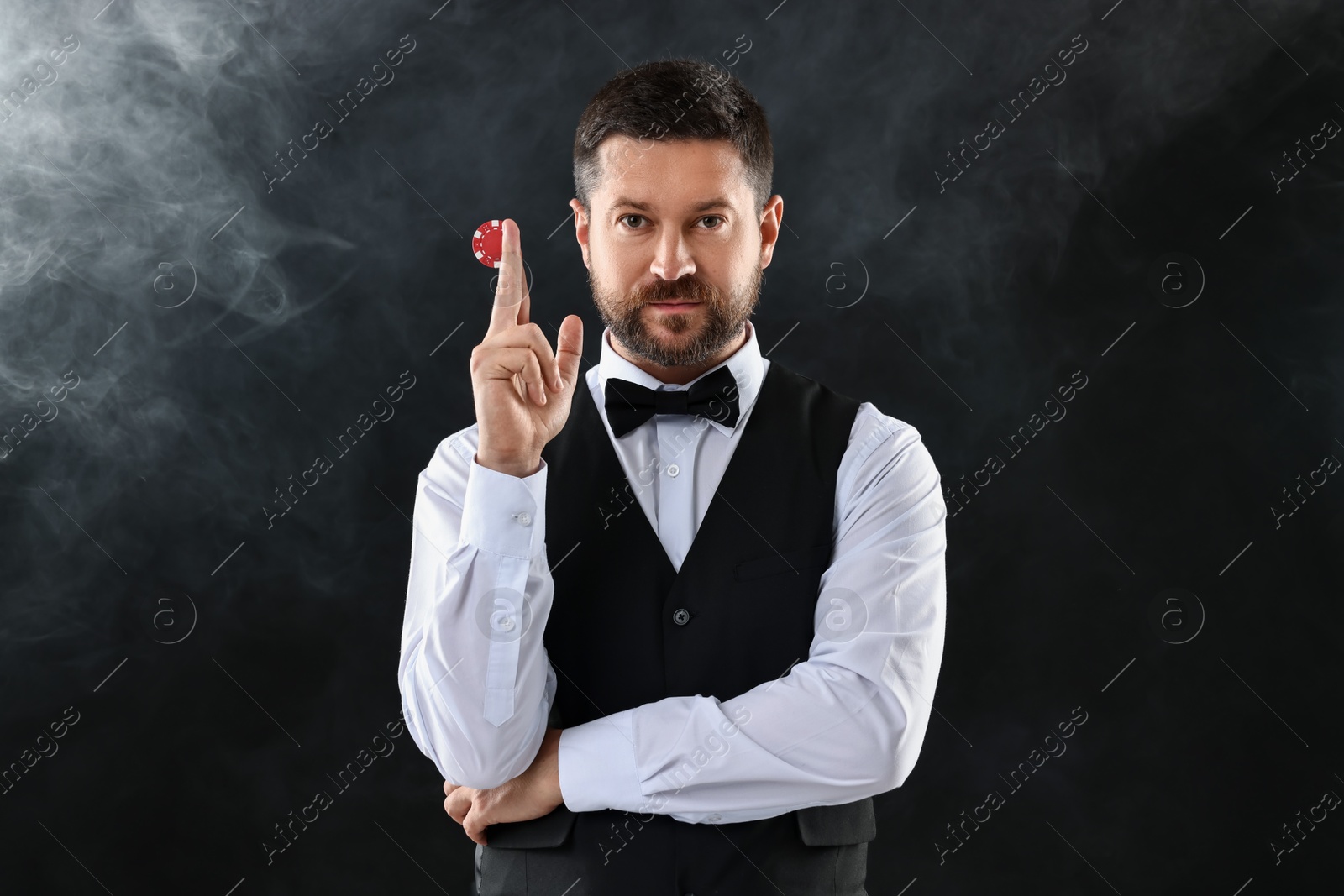 Photo of Croupier holding casino chip on black background with smoke