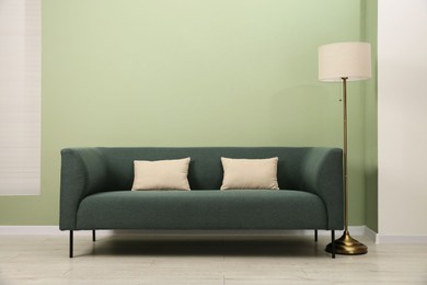 Photo of Stylish sofa with pillows and lamp near green wall indoors