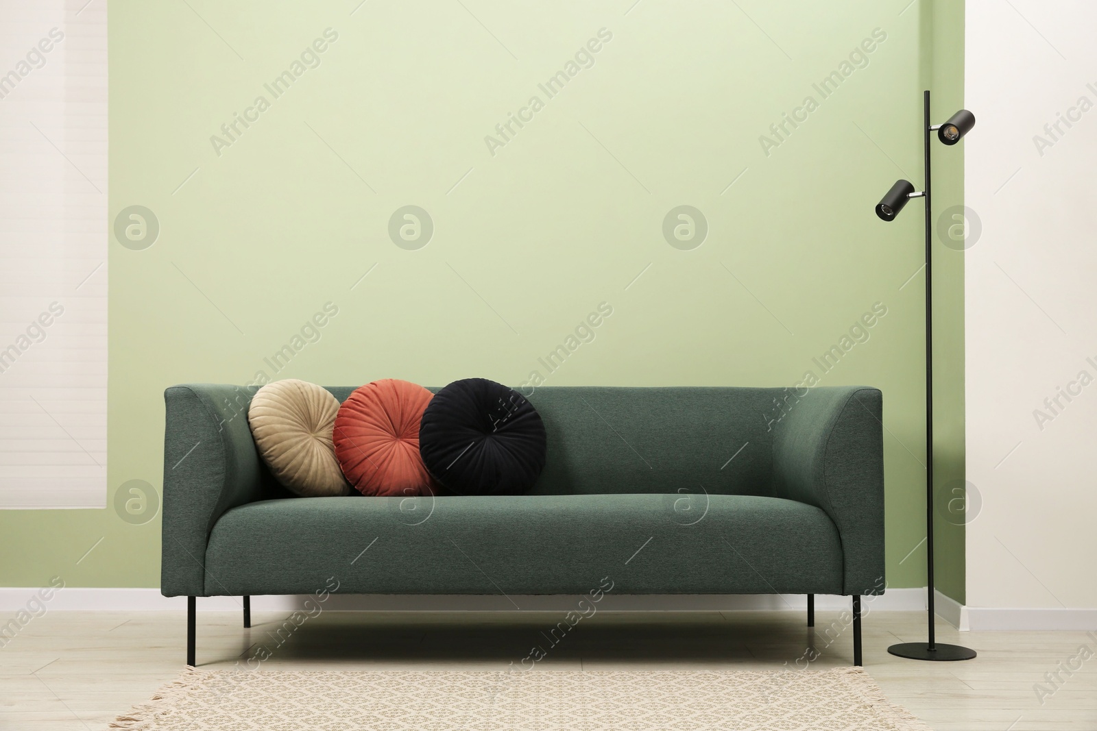 Photo of Stylish sofa with pillows and lamp near green wall indoors