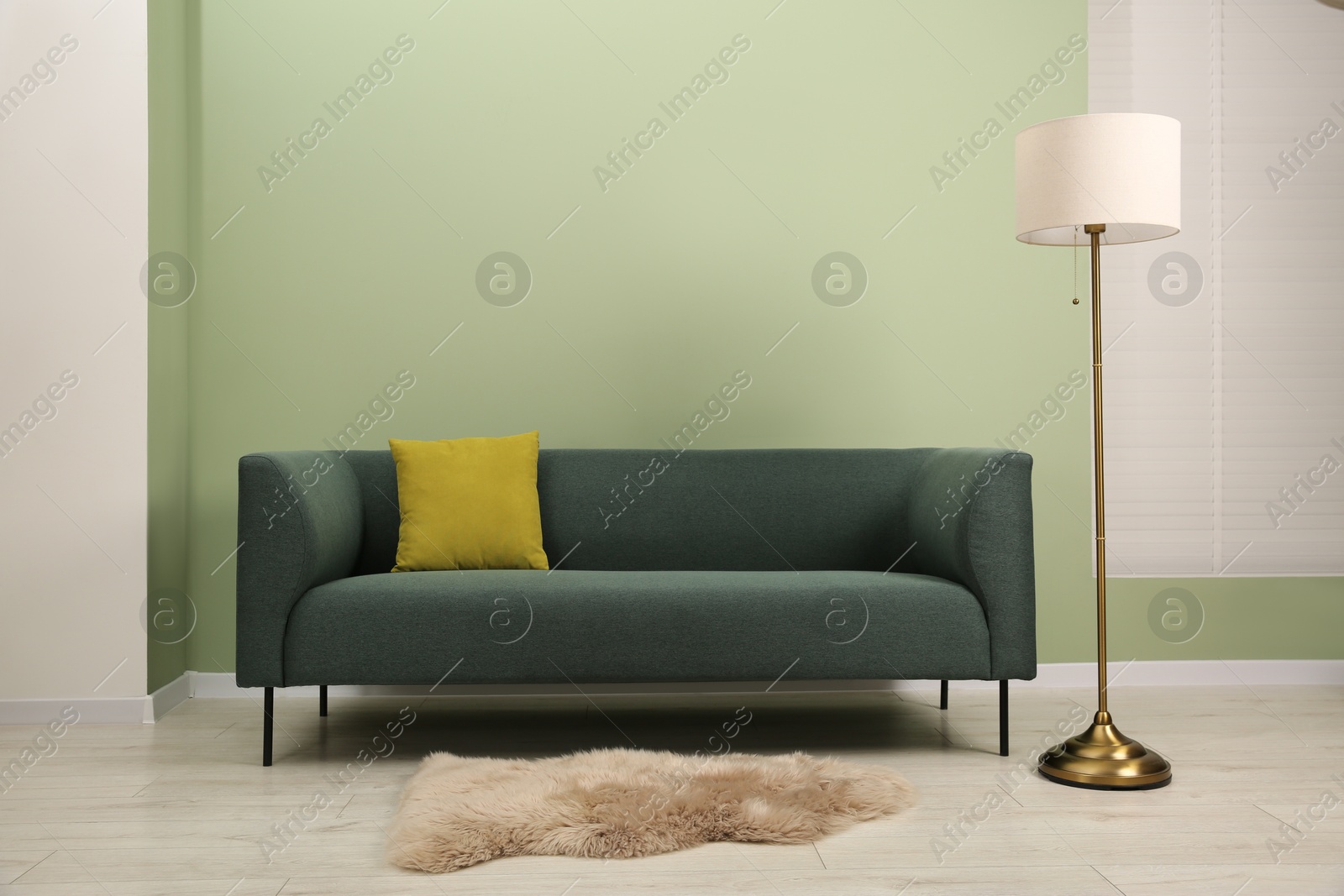 Photo of Stylish sofa with pillow and lamp near green wall indoors