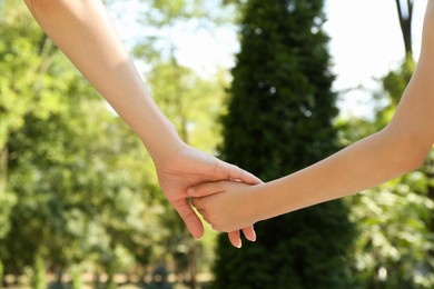 Photo of Mother and daughter holding hands in park, closeup