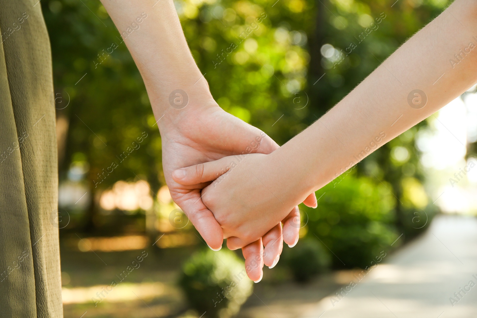 Photo of Mother and daughter holding hands in park, closeup