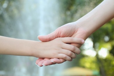 Photo of Mother and daughter holding hands in park, closeup