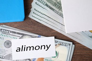 Photo of Alimony. Dollar banknotes, blank card and notebook on wooden table, top view