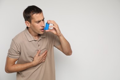 Man using asthma inhaler on light background, space for text