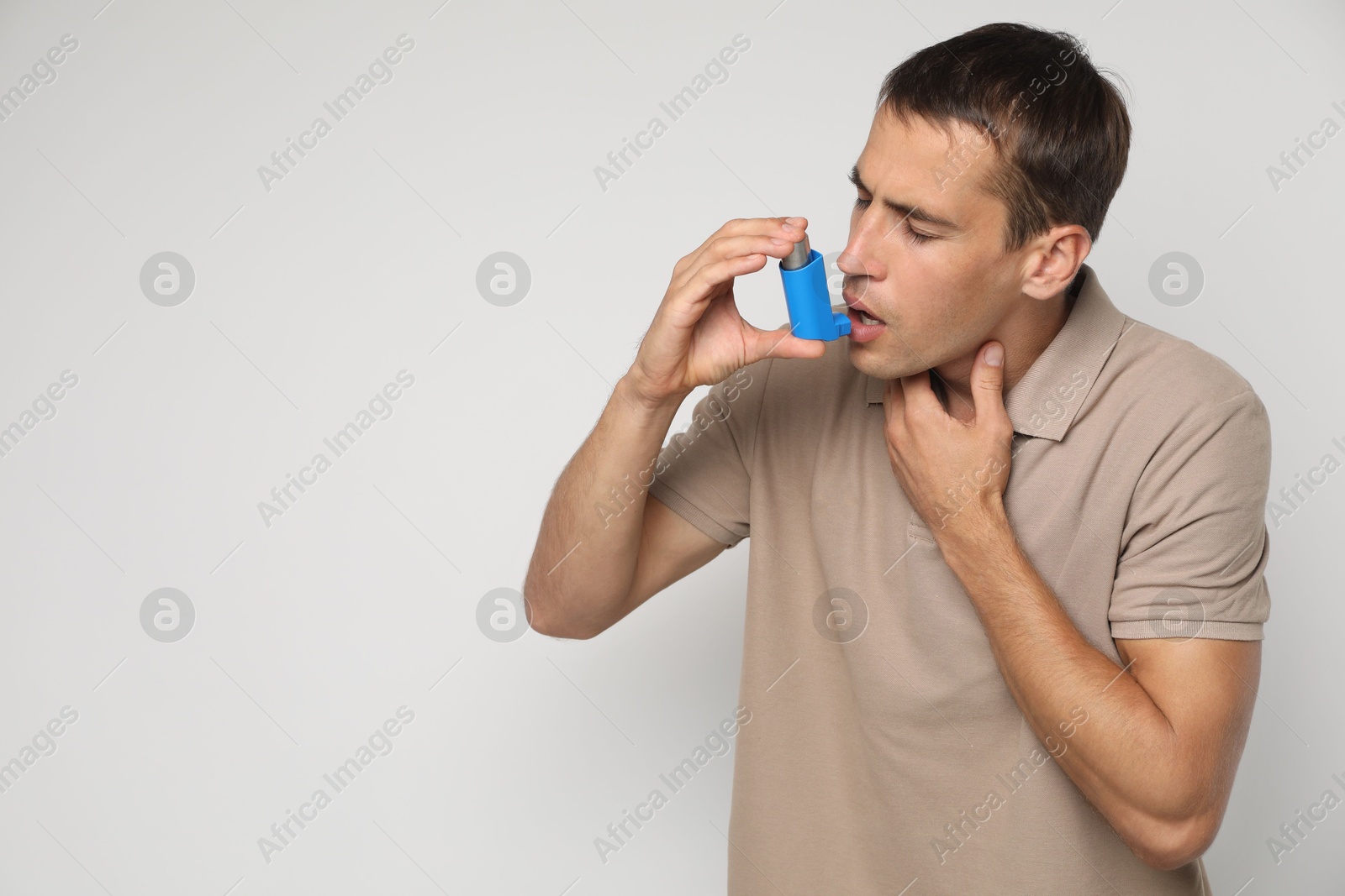 Photo of Man using asthma inhaler on light background, space for text