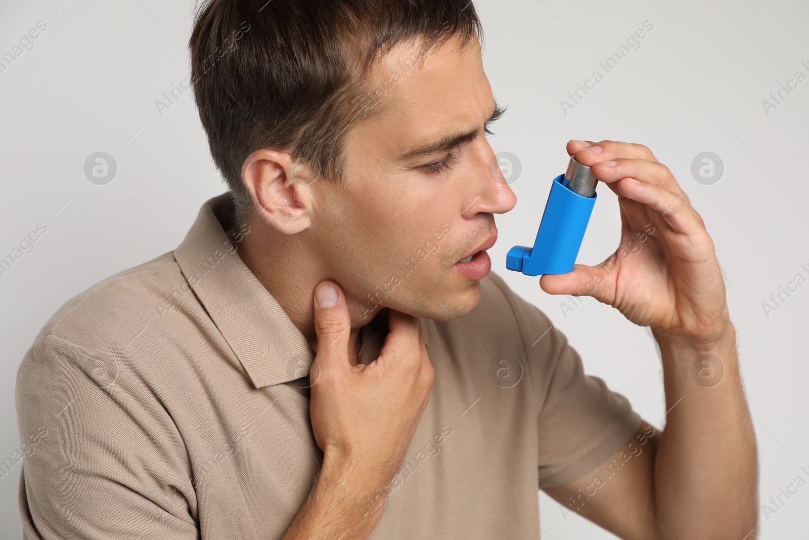 Photo of Man using asthma inhaler on light background