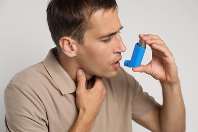 Man using asthma inhaler on light background