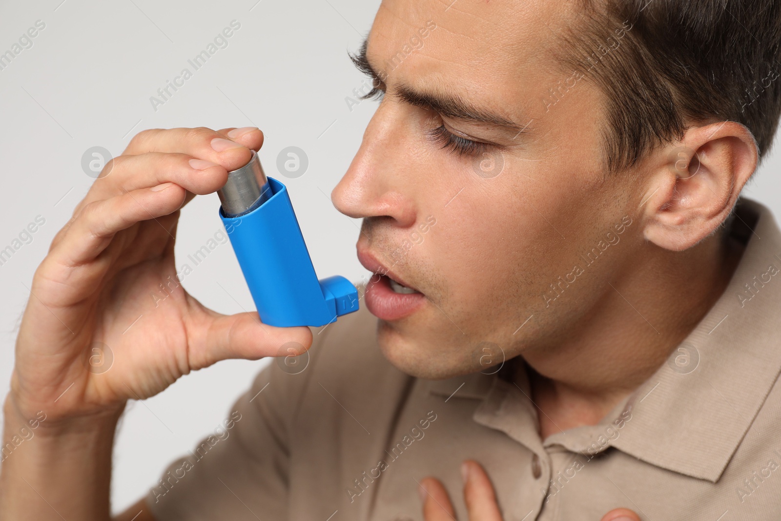 Photo of Man using asthma inhaler on light background, closeup