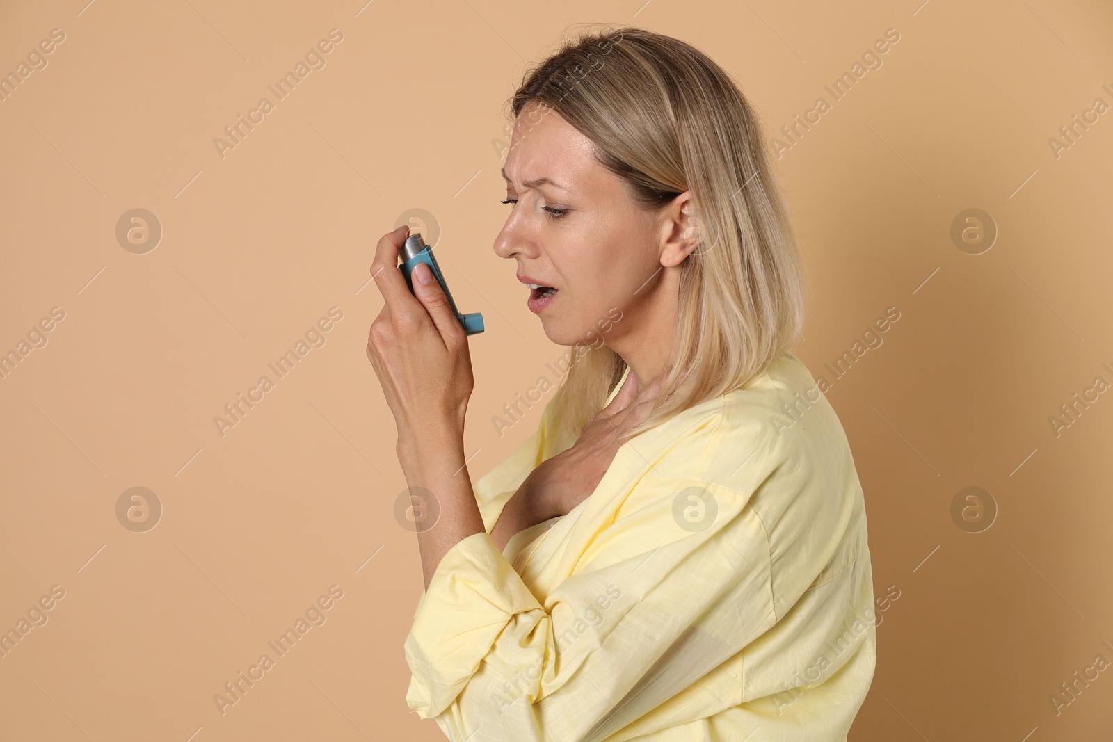 Photo of Woman using asthma inhaler on beige background