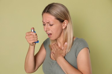 Photo of Woman using asthma inhaler on olive background