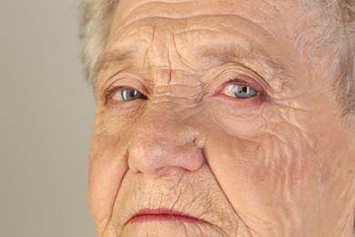 Senior woman with beautiful eyes on grey background, closeup