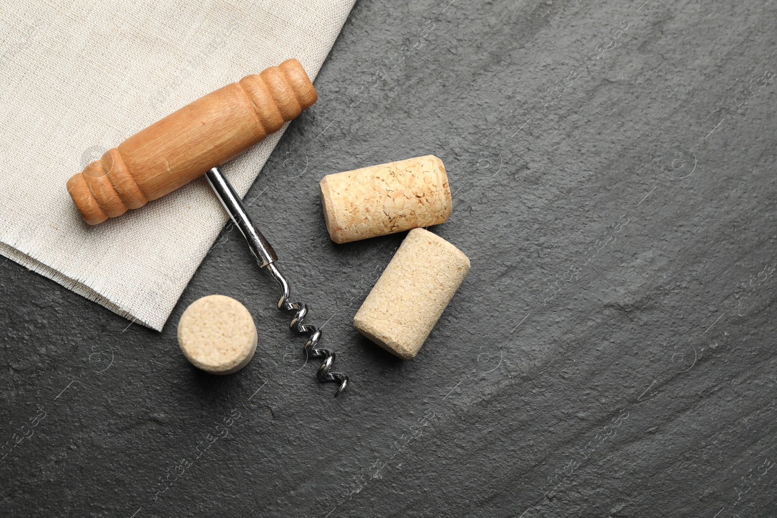 Photo of Corkscrew with wooden handle and corks on black table, top view. Space for text