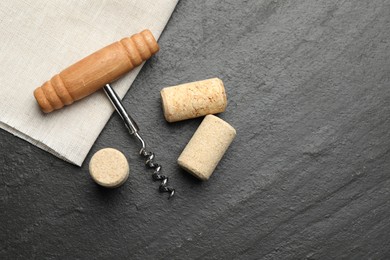 Corkscrew with wooden handle and corks on black table, top view. Space for text