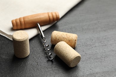 Photo of Corkscrew with wooden handle and corks on black table, closeup