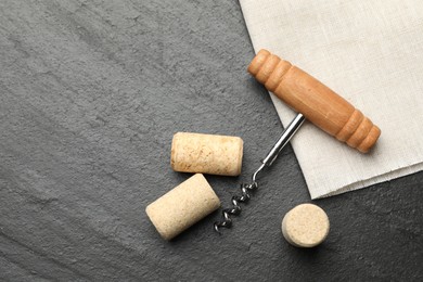 Corkscrew with wooden handle and corks on black table, top view. Space for text